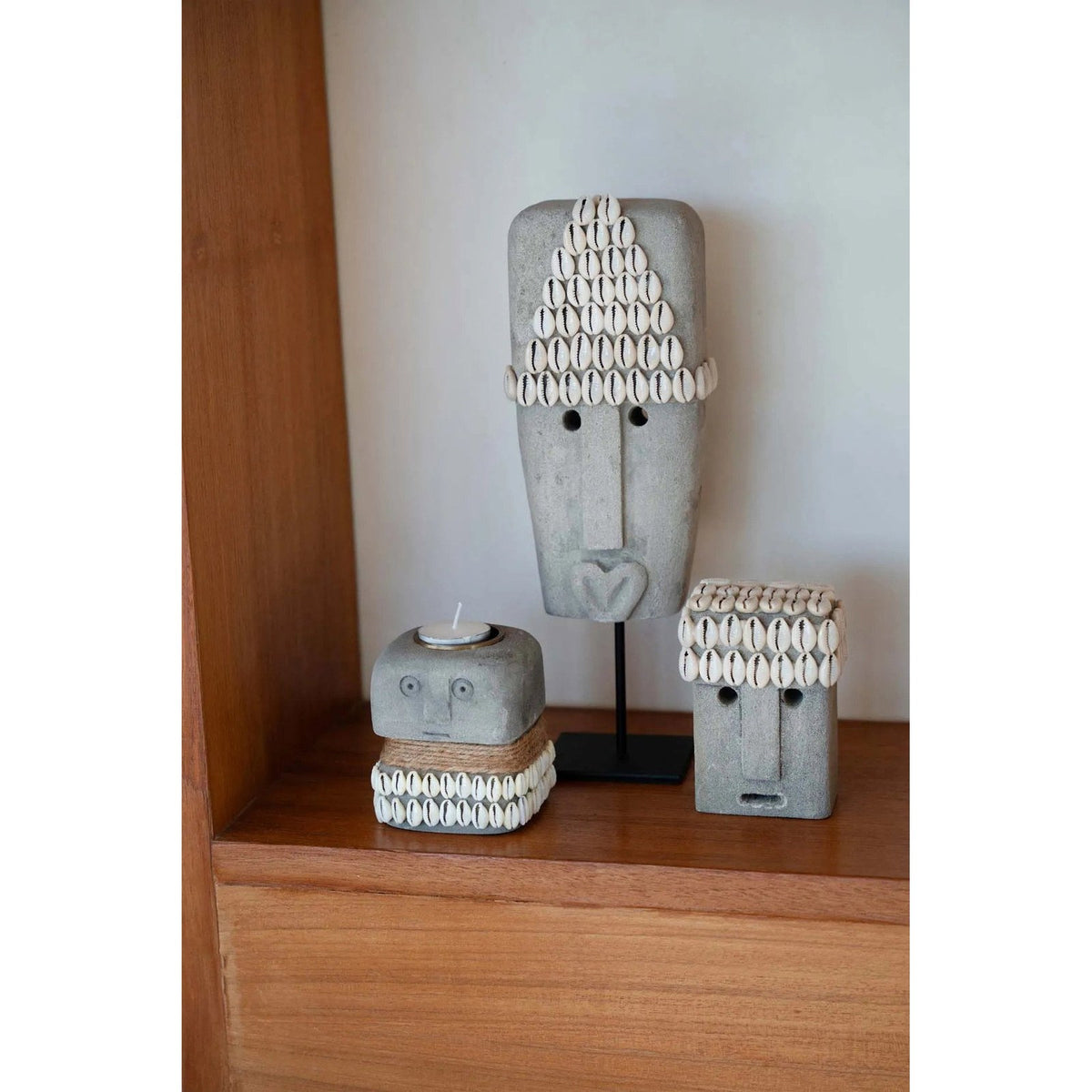 Tête décorative Sumba en grès gris posée sur une étagère en bois à côté d'un masque sur socle et d'un photophore