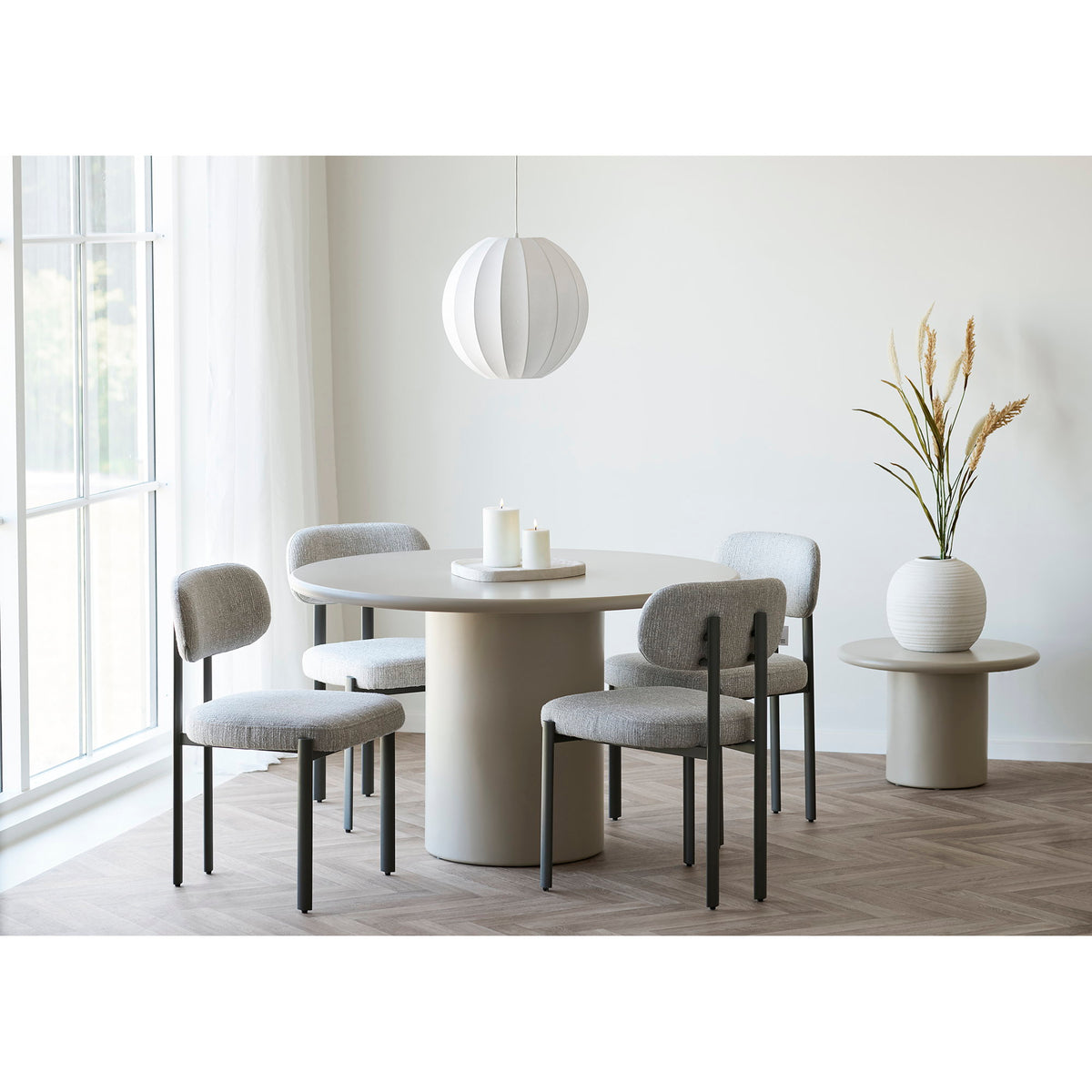 Vase boule blanc strié garni de graminées sur une table d'appoint près d'une table ronde et de chaises grises