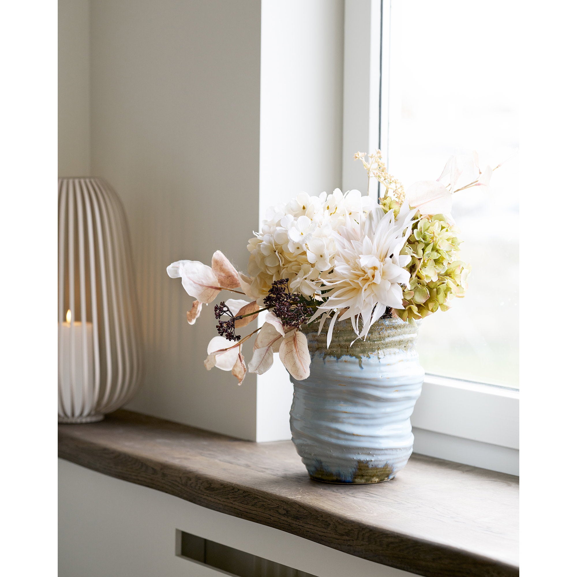 Vase céramique bleu glacier garni fleurs blanches hortensia posé rebord fenêtre bois