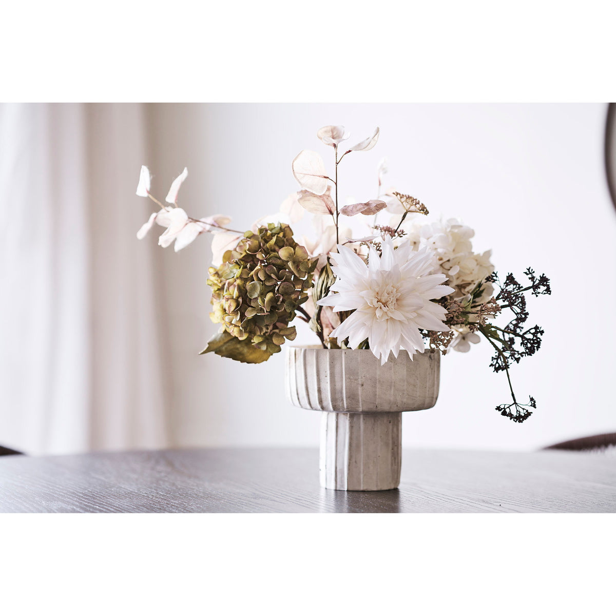 Vase coupe garni d'un bouquet d'hortensias et d'un dahlia clair sur une table en bois