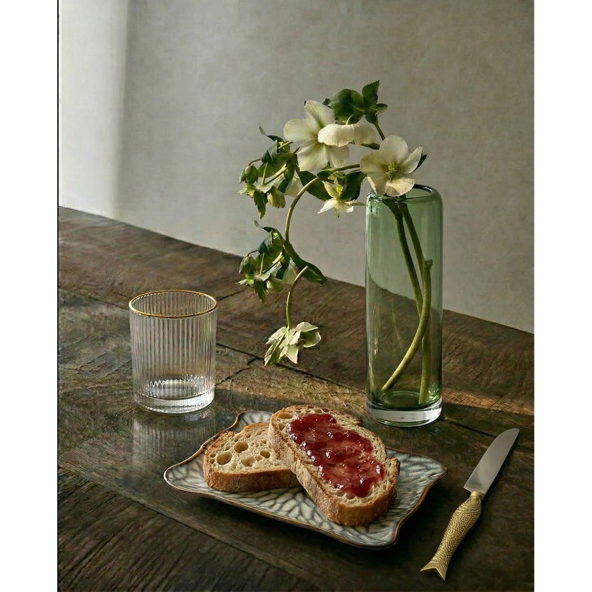 Vase Tall Vert garni d'hellébores blanches sur une table en bois sombre près d'un verre et de tartines