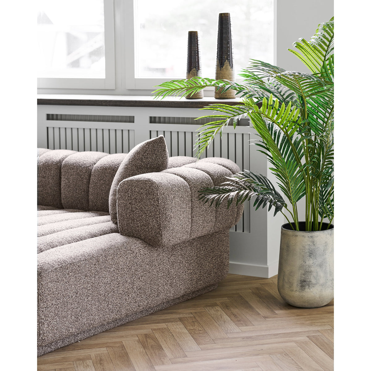 Duo de vases effilés brun tabac sur un rebord de fenêtre derrière un canapé bouclé et un palmier