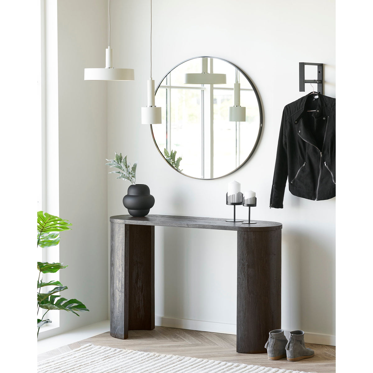 Vase noir mat avec une tige de feuillage sur une console en bois sombre sous un miroir rond