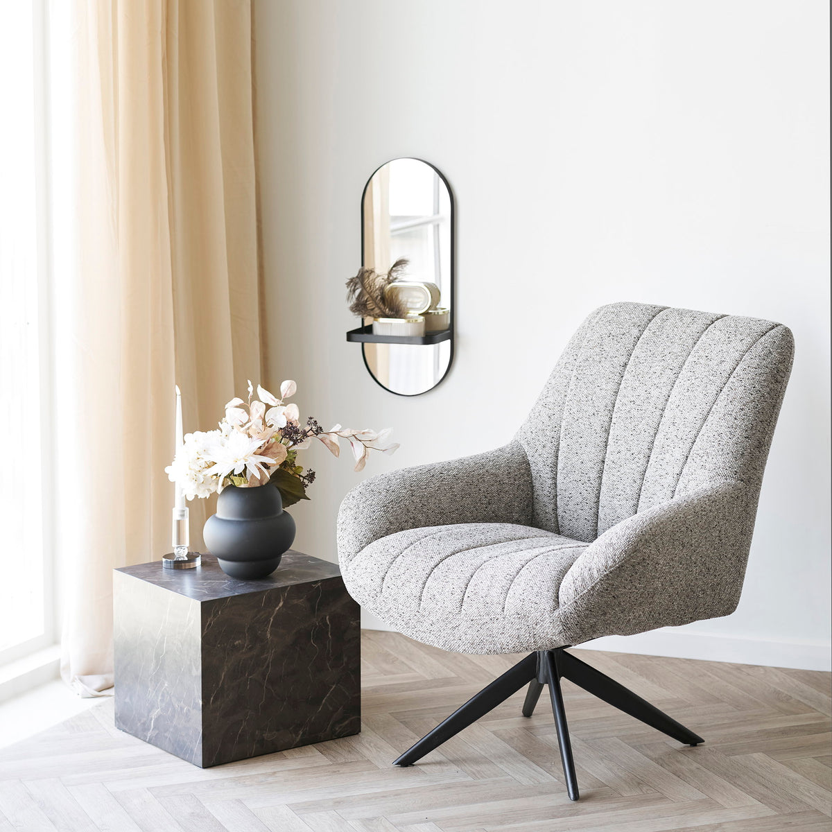 Vase noir mat avec un bouquet sur un cube effet marbre à côté d'un fauteuil chiné