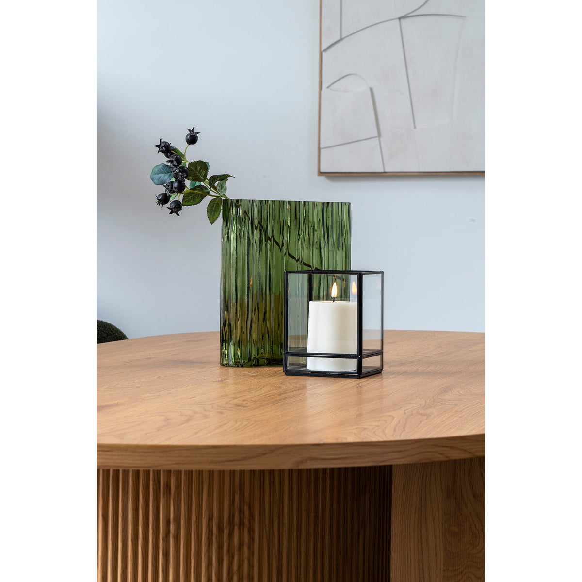 Vase vert fumé strié garni d'une branche de baies sur une table ronde en bois à côté d'une lanterne