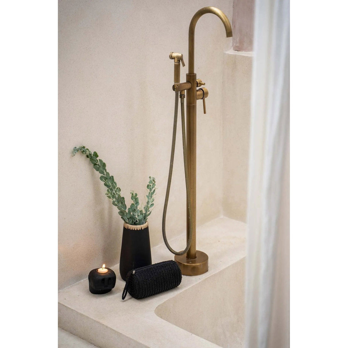 Vase Sneaky en terre cuite noire garni d'eucalyptus au bord d'une baignoire à côté d'un robinet en laiton