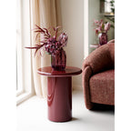 Vase verre soufflé rouge châtaigne garni fleurs bordeaux sur guéridon rouge salon bouclé
