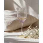 Verre à vin côtelé irisé rempli de vin blanc sur un linge clair près d'un bouquet de gypsophile