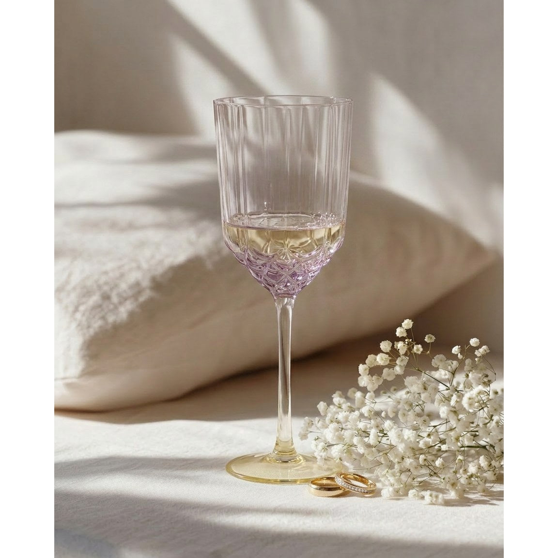 Verre à vin côtelé irisé rempli de vin blanc sur un linge clair près d'un bouquet de gypsophile