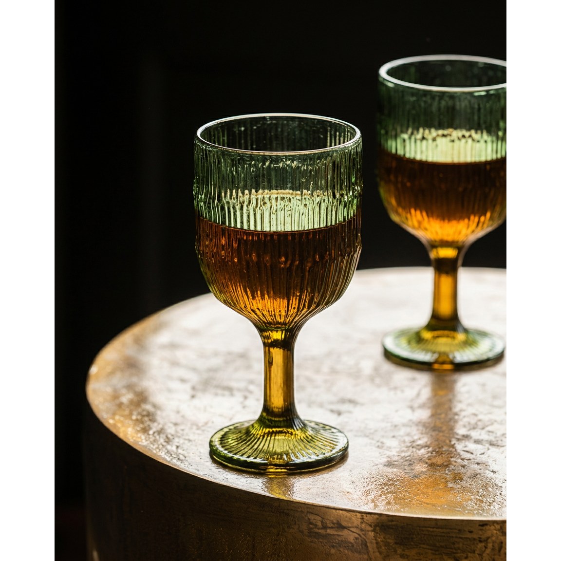 Deux verres à vin nervurés vert mousse remplis d'une boisson ambrée sur une table ronde dorée