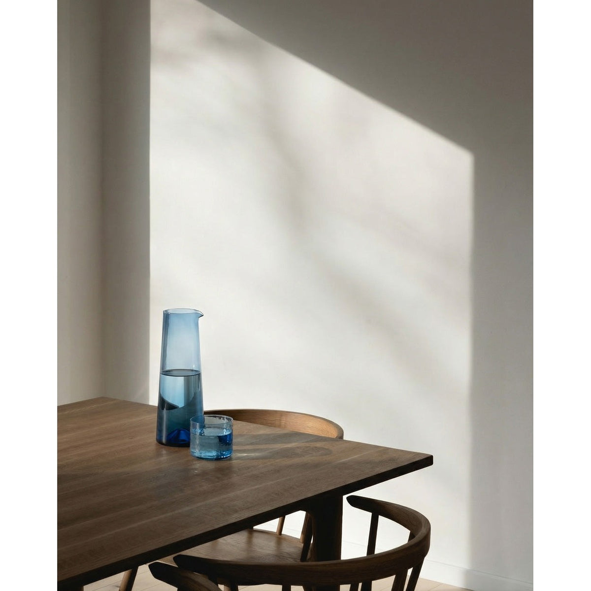 Verre bas martelé bleu sur une table en bois près d'une carafe bleue dans la lumière du jour