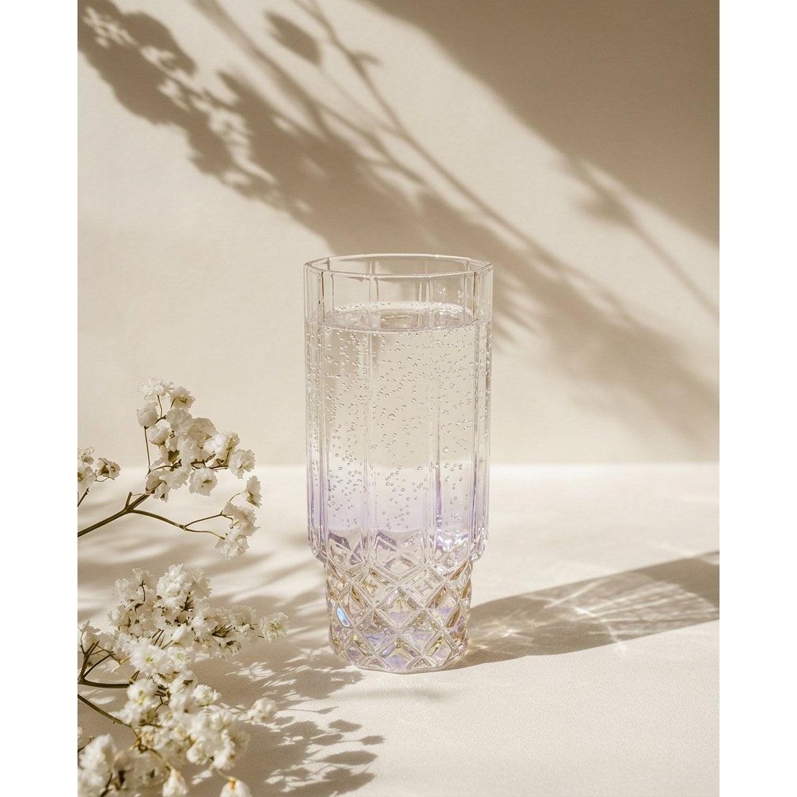 Verre highball irisé rempli d'eau pétillante près d'un bouquet de gypsophile blanche
